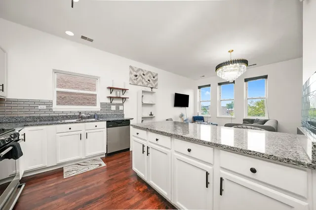 a large white kitchen with granite countertop a sink dishwasher a dining table and chairs with wooden floor