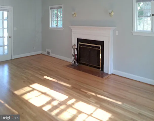 an empty room with wooden floor fireplace and windows
