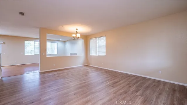 an empty room with wooden floor chandelier and windows