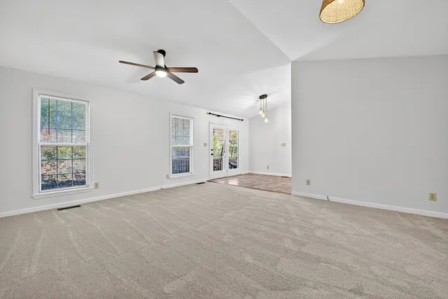 an empty room with chandelier fan and windows