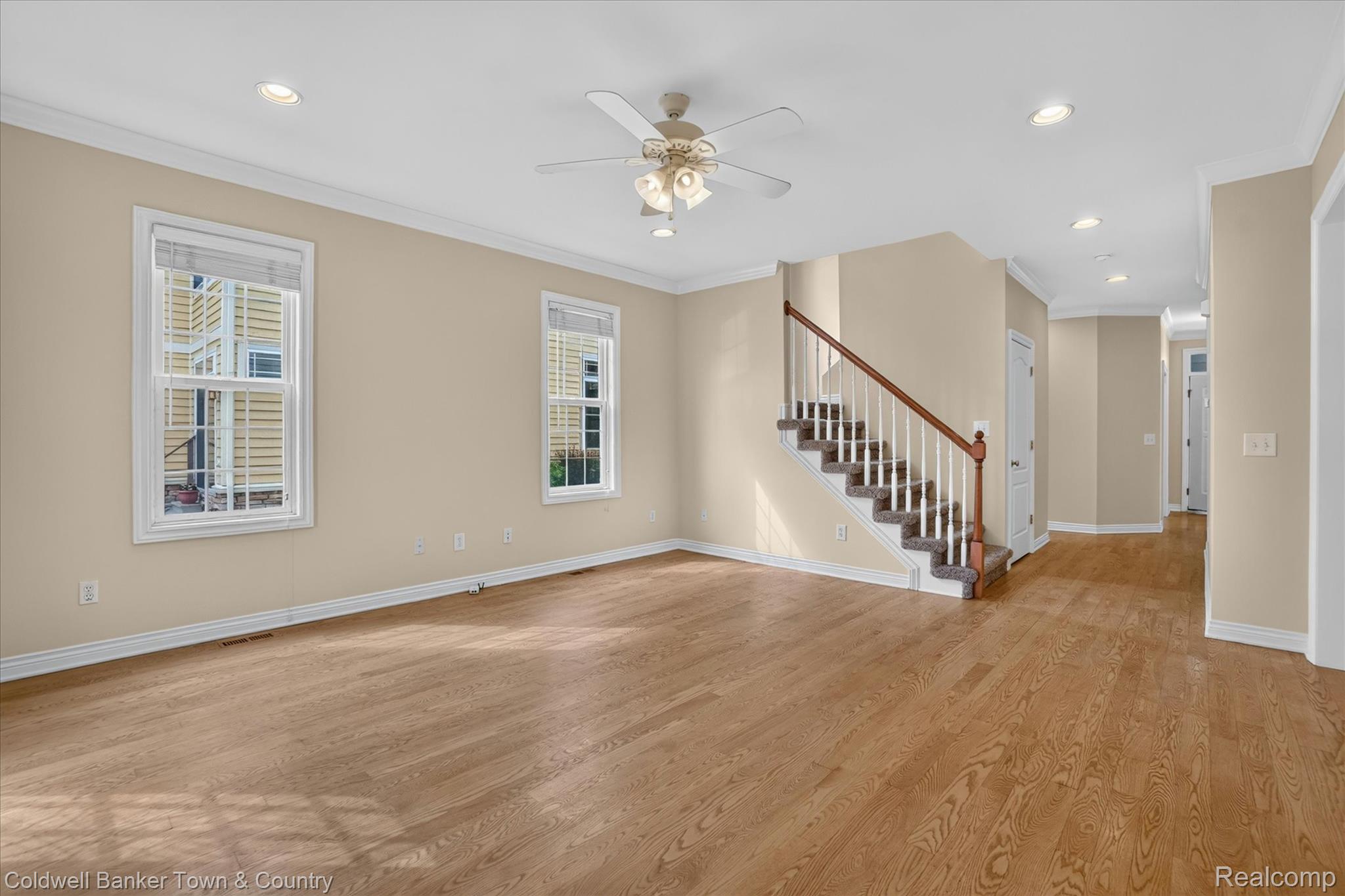 1725 Town Commons Drive Howell, MI 48855 - Photo 25 of 53 Spacious interior featuring wood-finish flooring, two large windows, a staircase with wood newel posts and handrails, a ceiling fan with integrated lighting, and recessed ceiling lights