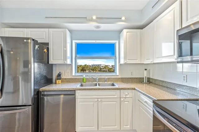 a kitchen with stainless steel appliances granite countertop a sink a refrigerator and white cabinets