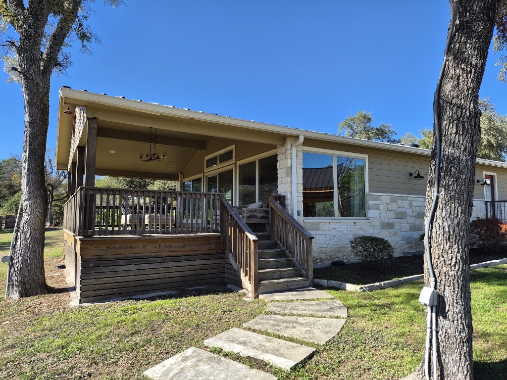 View of front facade with stone siding, a front lawn, a metal roof, stairs, and a wooden deck