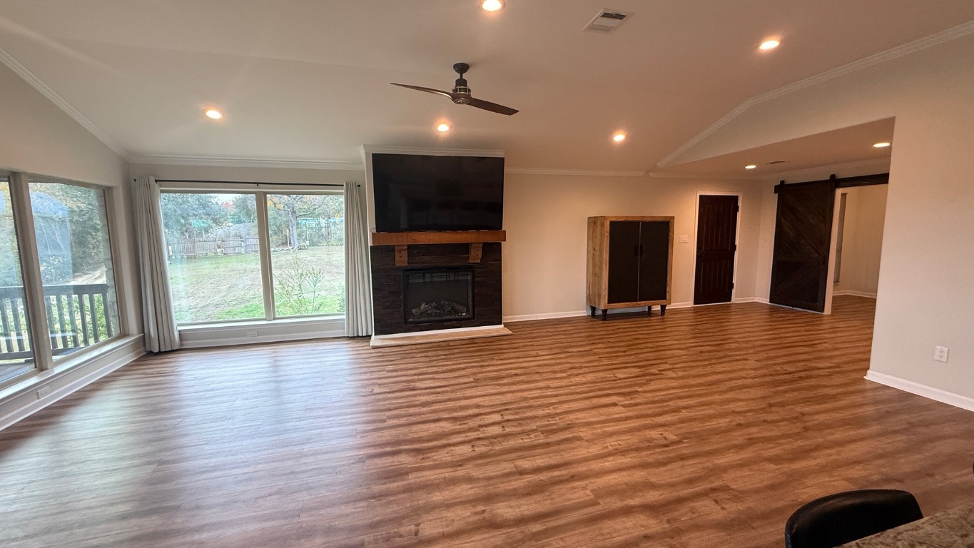 12987 Farm To Market Road 2769 Austin, TX 78726 - Photo 3 of 24 Unfurnished living room featuring vaulted ceiling, a barn door, crown molding, a fireplace, and wood finished floors