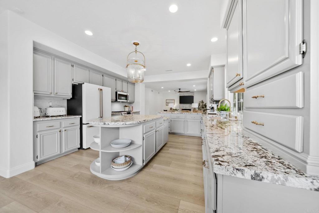 31401 Chemin Chevalier Temecula, CA 92591 - Photo 5 of 74 a large white kitchen with kitchen island a stove a sink a refrigerator and white cabinets with wooden floor