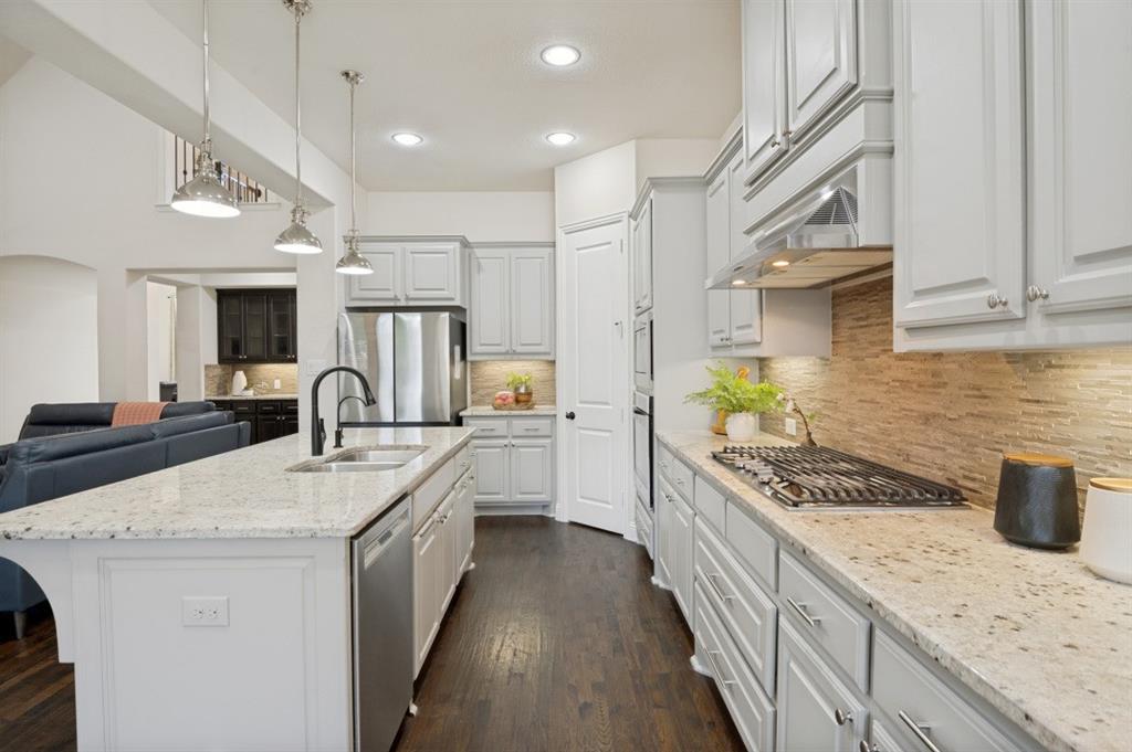 14215 Raspberry Lane Frisco, TX 75035 - Photo 7 of 30 Spacious kitchen featuring an expansive center island with a double basin sink and matte black faucet, light-toned countertops, stainless steel appliances, a gas cooktop, and light gray cabinetry