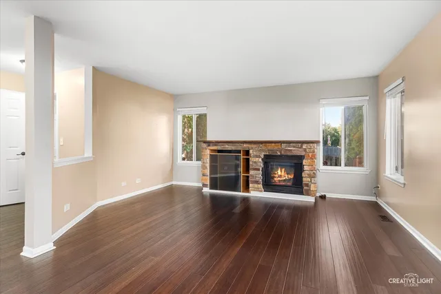 an empty room with wooden floor fireplace and windows