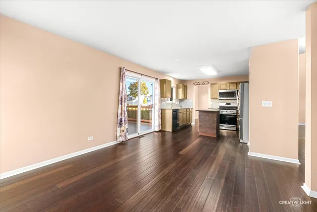 a view of a kitchen and an empty room with wooden floor and windows