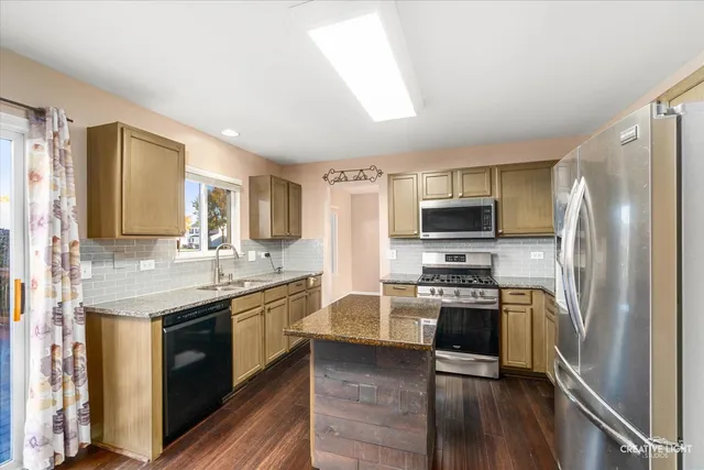 a kitchen with stainless steel appliances granite countertop a stove top oven a sink and dishwasher a refrigerator with wooden floor