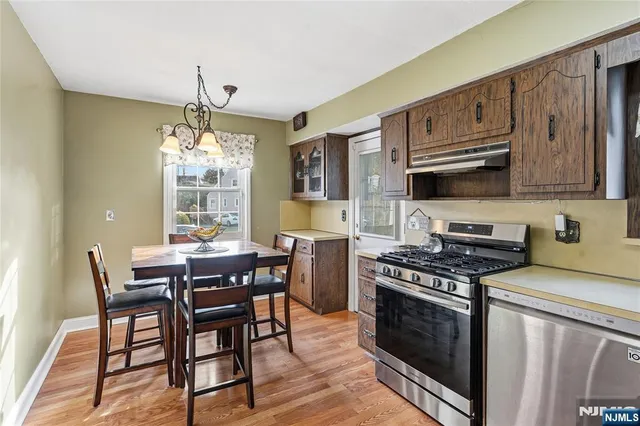 a kitchen with stainless steel appliances a stove a sink dishwasher a dining table and chairs with wooden floor