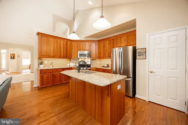 a kitchen with stainless steel appliances granite countertop a sink a stove a refrigerator a center island with wooden floor and cabinets