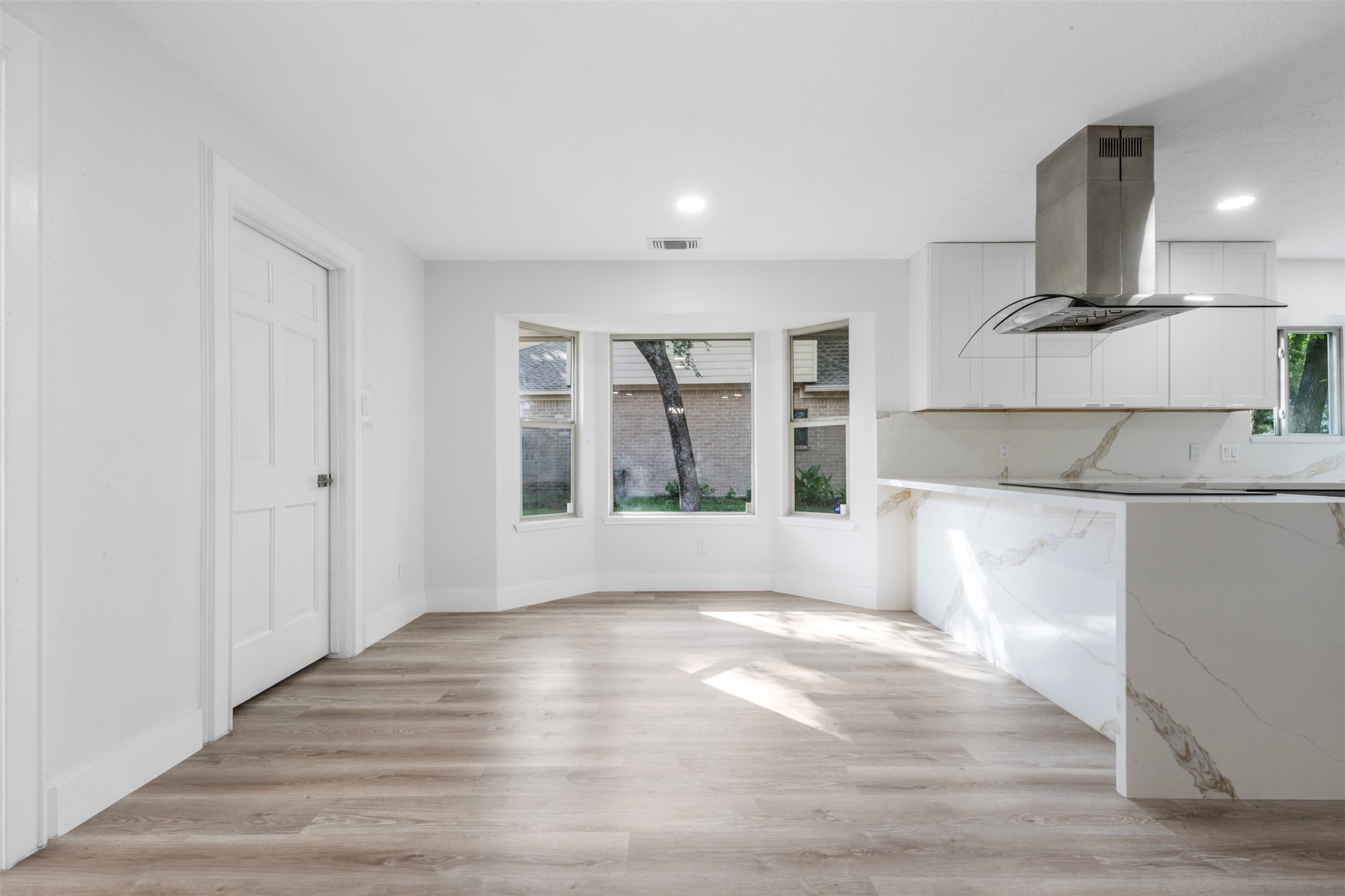 9543 Enstone Circle Spring, TX 77379 - Photo 11 of 50 Bright and spacious open-plan room with light wood flooring, large bay windows, and a modern kitchen featuring sleek white cabinetry and marble accents.