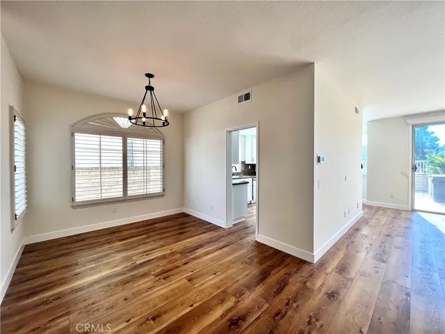 an empty room with wooden floor chandelier and windows