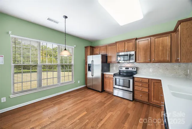 a kitchen with stainless steel appliances granite countertop a refrigerator a sink dishwasher a stove and white countertops with wooden floor