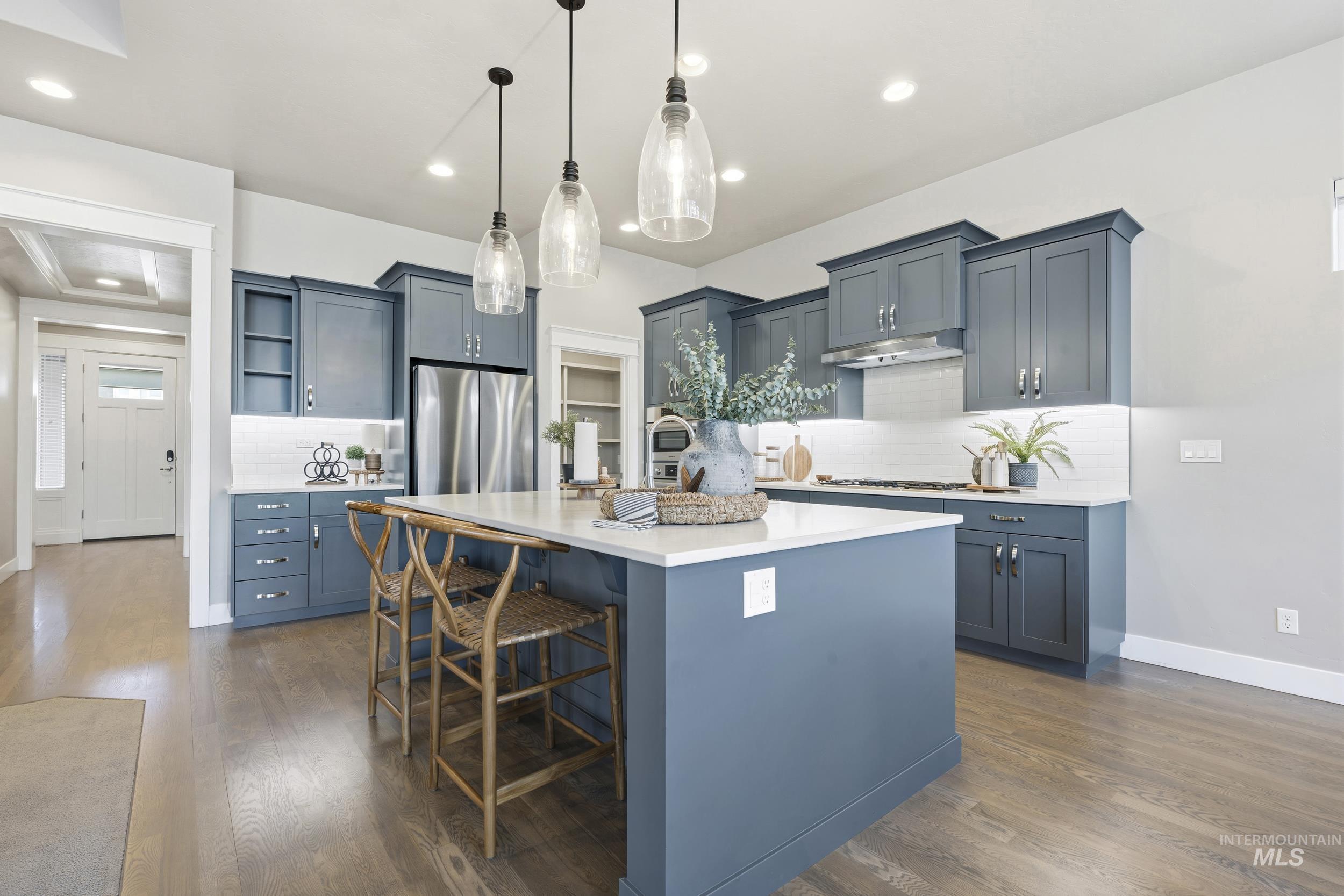5699 North Fairborn Avenue Meridian, ID 83646 - Photo 9 of 30 Kitchen featuring hanging light fixtures, an island with sink, a kitchen breakfast bar, tasteful backsplash, and dark wood-type flooring