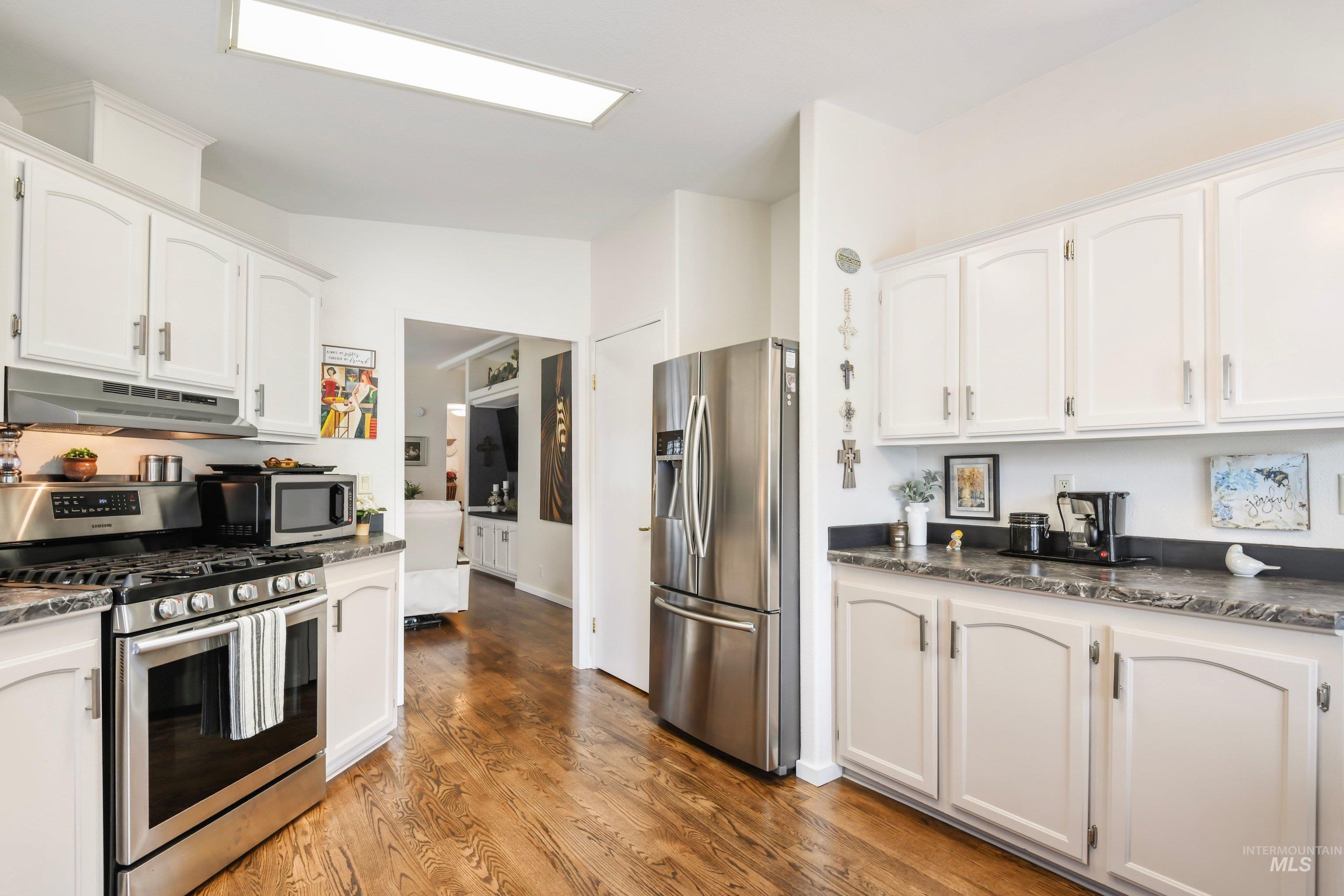 421 South Curtis Road, Unit 202 202 Boise, ID 83705 - Photo 13 of 41 Kitchen featuring wood-finish flooring, white cabinetry, dark stone-finish countertops, stainless steel appliances, and a dining nook with bay windows