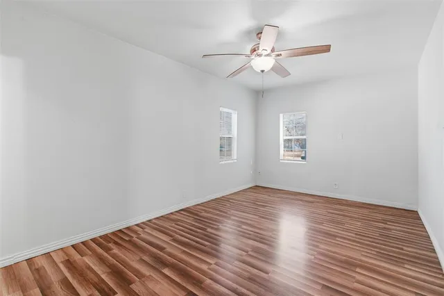 an empty room with wooden floor fan and windows