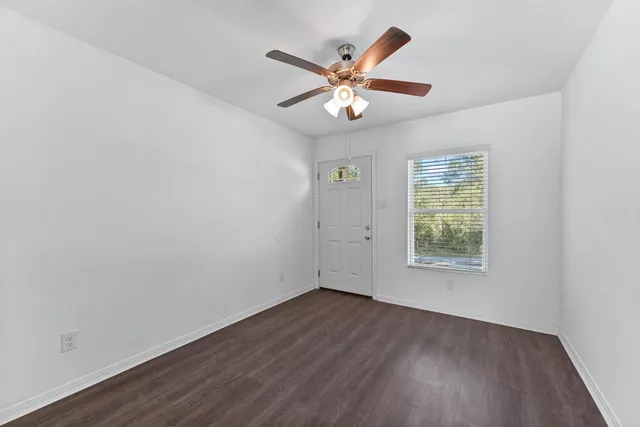 an empty room with wooden floor fan and windows