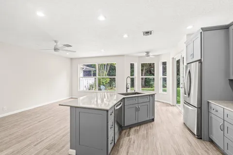a large kitchen with kitchen island a large window a sink stainless steel appliances and cabinets