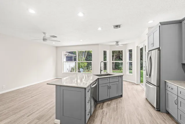 a large kitchen with kitchen island a large window a sink stainless steel appliances and cabinets