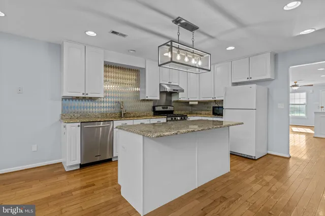 a kitchen with stainless steel appliances granite countertop a sink a stove a refrigerator and island with wooden floor