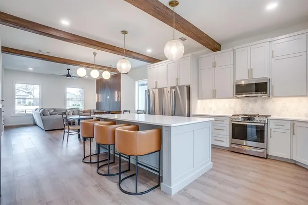 a kitchen with stainless steel appliances granite countertop a stove top oven a sink dishwasher a dining table and chairs with wooden floor