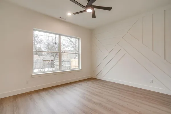 an empty room with wooden floor fan and windows