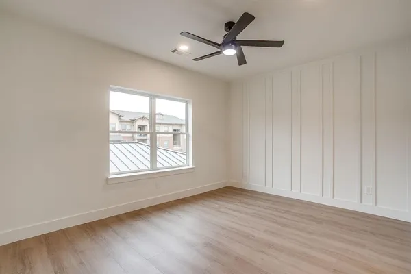 an empty room with wooden floor fan and windows