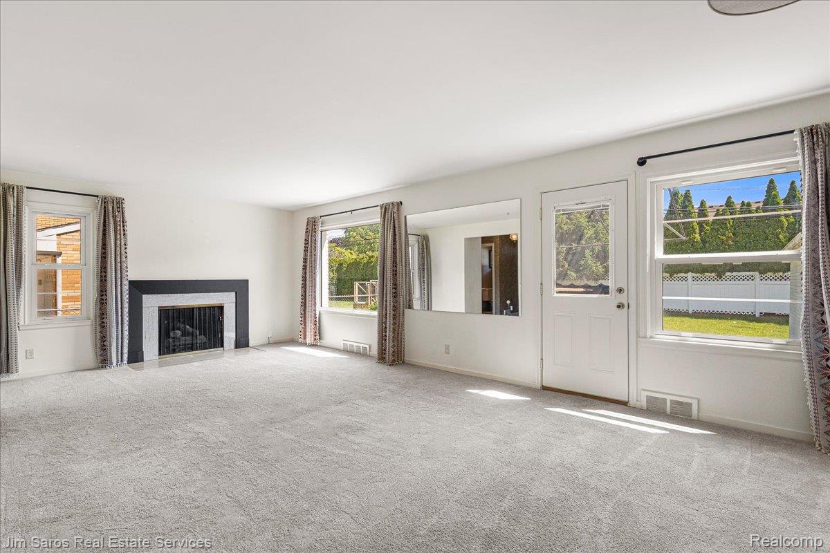 1010 Nottingham Road Grosse Pointe, MI 48230 - Photo 6 of 30 Spacious interior featuring light gray carpeting, multiple windows, a central fireplace with a dark surround, white walls, and a glass-paneled exterior door