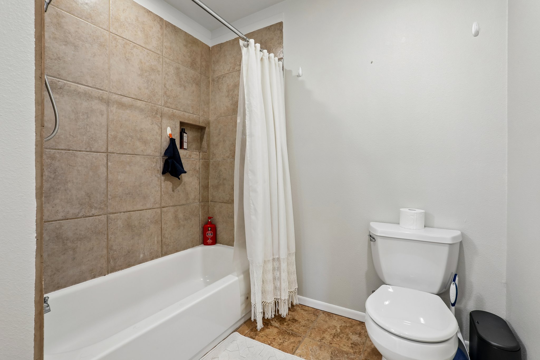 1114 West 2nd Street Elgin, TX 78621 - Photo 19 of 31 Functional bathroom features a clean white tub and toilet, with practical tile surrounding the bathing area.