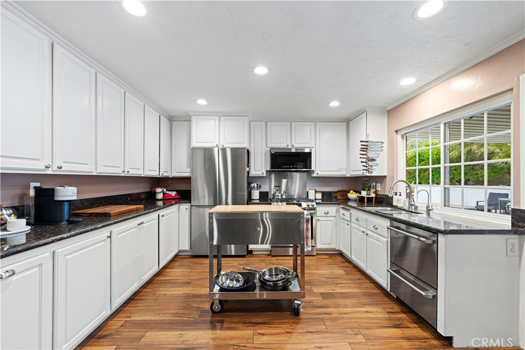 23255 Redbud Ridge Circle Valencia, CA 91354 - Photo 10 of 19 a kitchen with granite countertop a stove top oven a sink dishwasher a refrigerator and white cabinets with wooden floor
