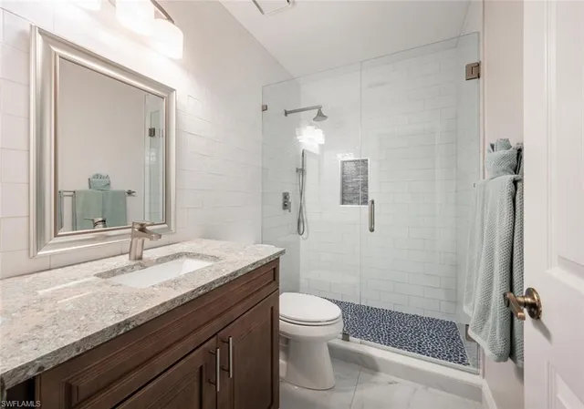 a bathroom with a granite countertop sink a toilet a mirror and shower