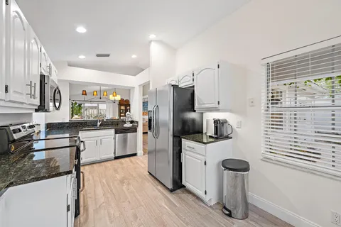 a kitchen with stainless steel appliances kitchen island granite countertop a refrigerator oven a sink dishwasher and white cabinets with wooden floor