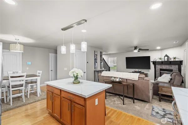 a kitchen with stainless steel appliances kitchen island granite countertop a stove a refrigerator a sink a dining table and chairs with wooden floor