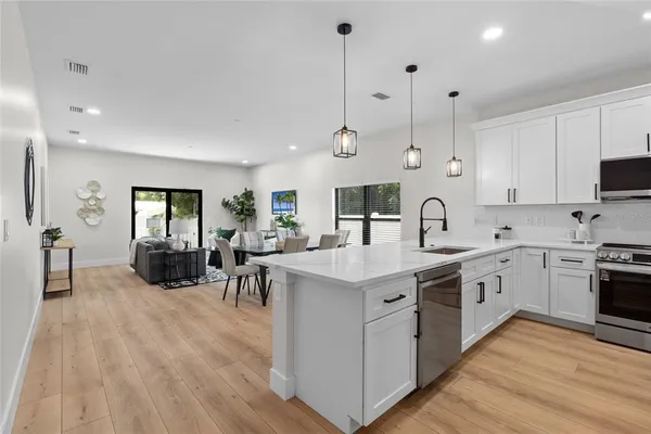 a kitchen with stainless steel appliances granite countertop a stove top oven a sink dishwasher a dining table and chairs with wooden floor