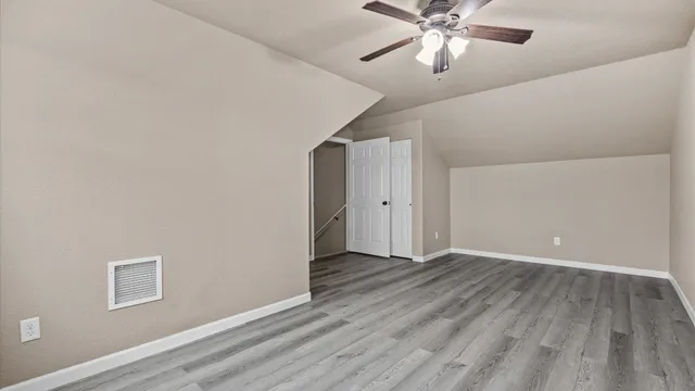 a view of an empty room with wooden floor and a ceiling fan