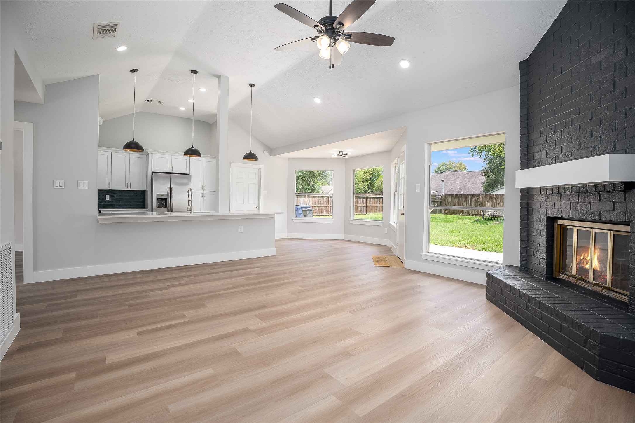 1406 Kent Way Friendswood, TX 77546 - Photo 6 of 31 an empty room with wooden floor a kitchen view and a fireplace