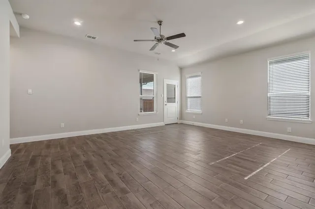 an empty room with wooden floor ceiling fan and windows