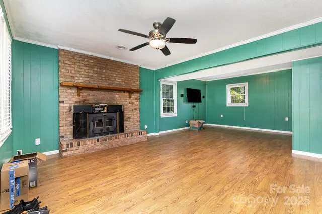 a view of a livingroom with a fireplace a ceiling fan and a kitchen view