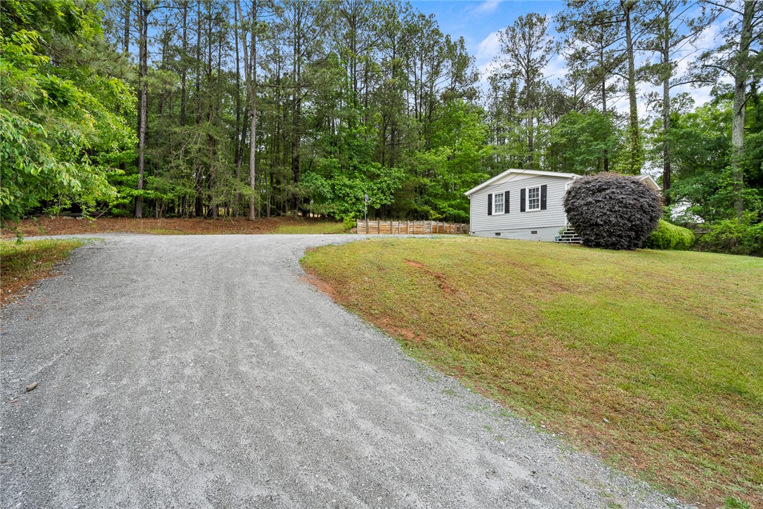 111 State Rd S-4-104 Anderson, SC 29626 - Photo 25 of 42 A winding gravel driveway leads to a charming residence nestled amidst a lush, wooded landscape.