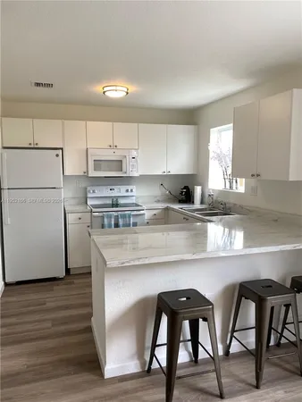 a kitchen with stainless steel appliances granite countertop a stove a sink dishwasher a refrigerator white cabinets with wooden floor