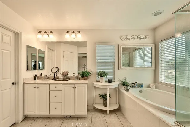 a bathroom with a double vanity sink a mirror a bathtub and next to a window