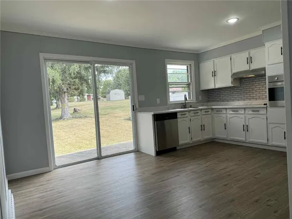 a large kitchen with stainless steel appliances granite countertop a stove a sink and white cabinets with wooden floor