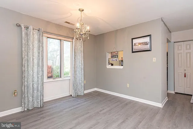 an empty room with wooden floor chandelier and windows