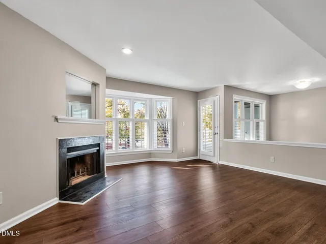 a view of an empty room with wooden floor fireplace and a window