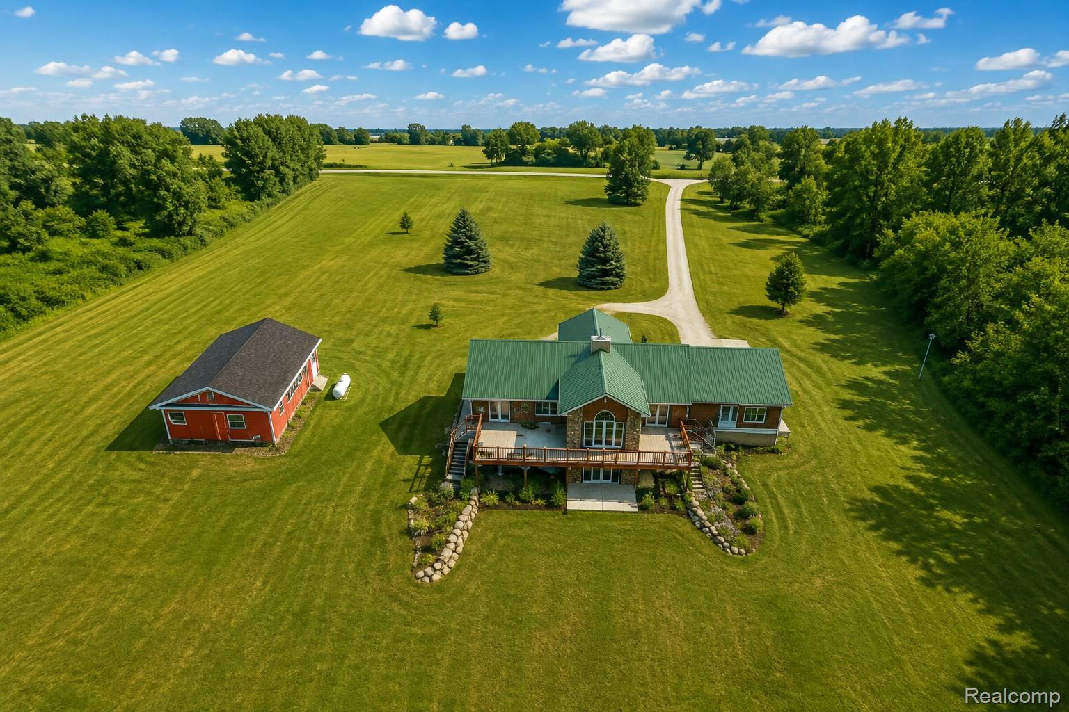 7542 Newberry Road Durand, MI 48429 - Photo 2 of 25 Expansive green property featuring a red outbuilding, a gravel driveway, mature trees, and a house with a green metal roof
