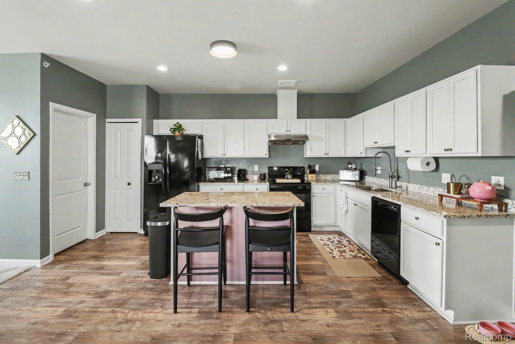 9864 Ridge Run Street Howell, MI 48855 - Photo 12 of 23 Kitchen featuring black appliances, light stone counters, white cabinetry, a breakfast bar area, and a center island