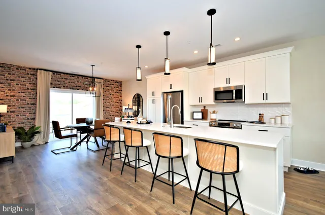 a kitchen with stainless steel appliances granite countertop a stove a refrigerator a kitchen island a dining table and chairs with wooden floor