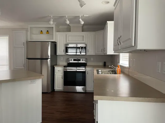 a kitchen with stainless steel appliances a refrigerator a stove a sink and white cabinets