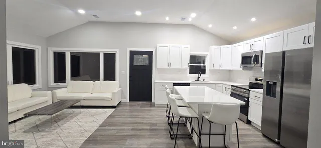 a kitchen with stainless steel appliances kitchen island granite countertop a refrigerator a stove and a dining table with wooden floor